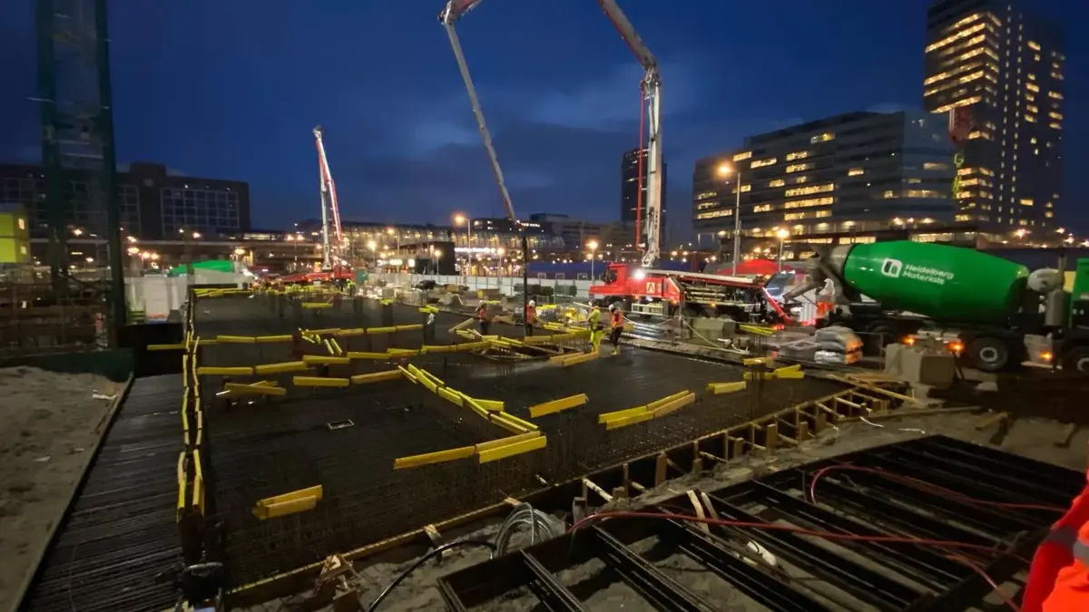 Bouwplaats bij schemering met betonpomp en mixer over dekwapening en bekisting