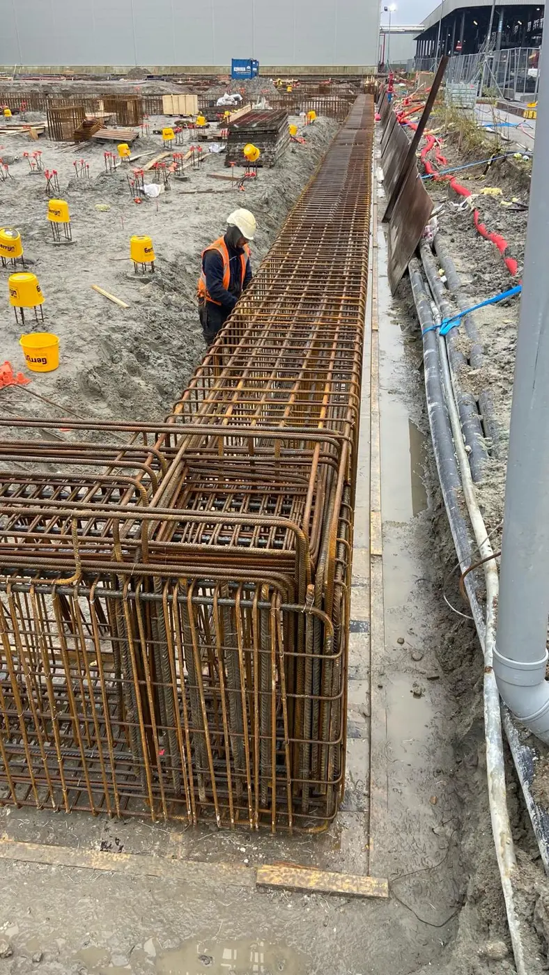 Vlechter van MME Bouw bindt de wapeningskorven van een lange funderingsbalk op de bouwplaats