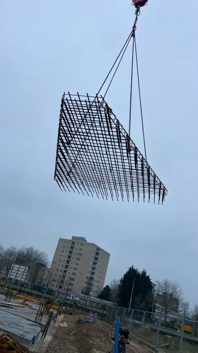 Lange wapeningskorf gehesen door kraan voor brugconstructie